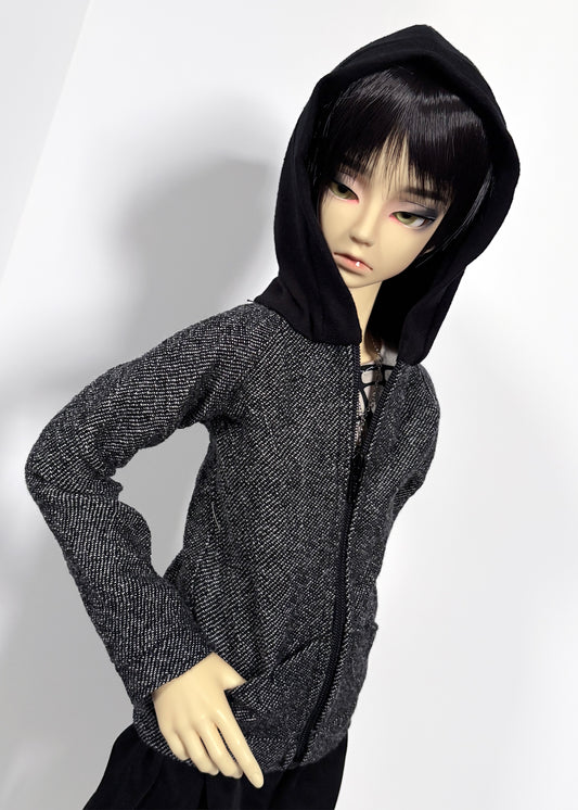 A doll wearing a black hooded zip-up jacket with a textured gray and black wool body, posed against a plain light background.