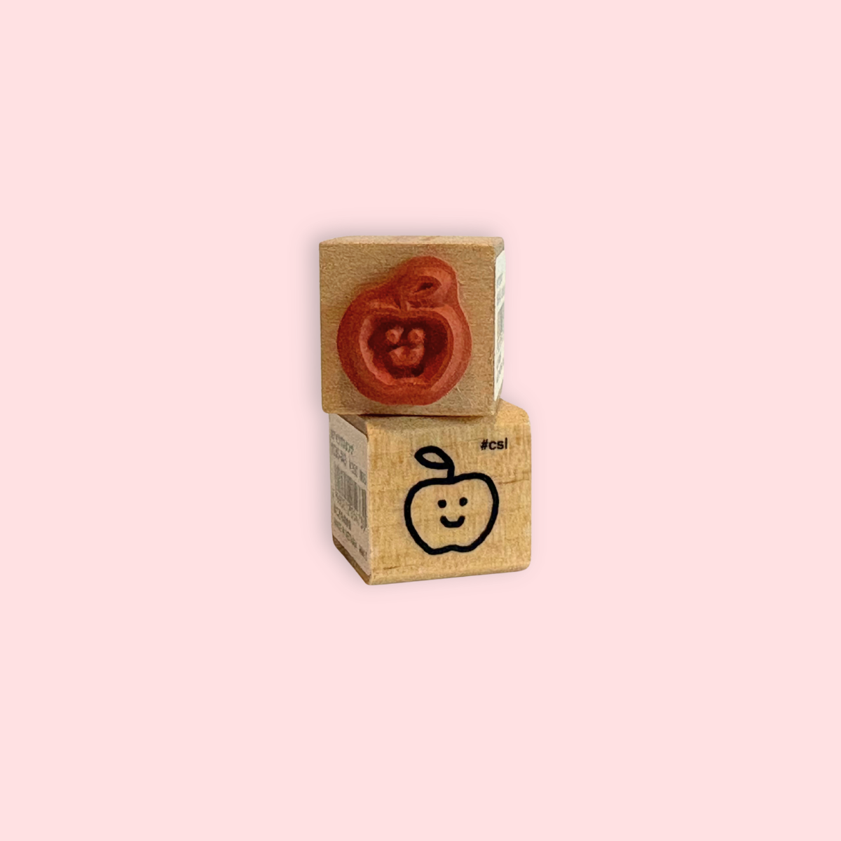 Little Happy Apple Rubber Stamp showing a cute apple face design on a wooden block with pink background