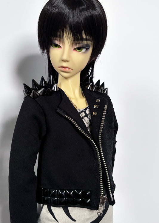 A doll with short black hair and pale skin wearing a black studded jacket with black metal details, photographed against a plain light background.