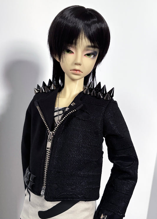 A doll with short black hair wearing a black textured zip-front jacket with spiked shoulders, paired with a patterned shirt and light bottoms, photographed against a plain light background.