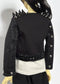 A doll with short black hair and pale skin wearing a black studded jacket with black metal details, photographed against a plain light background.