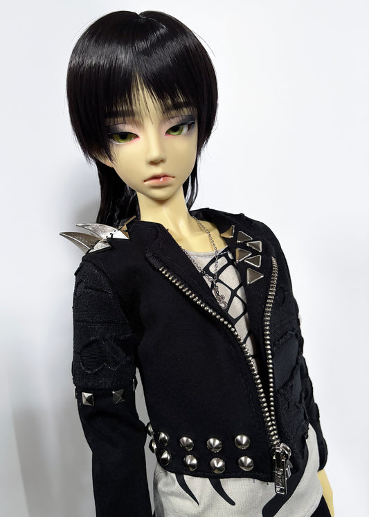 A doll with short black hair and pale skin wearing a black studded jacket with silver metal details, photographed against a plain light background.