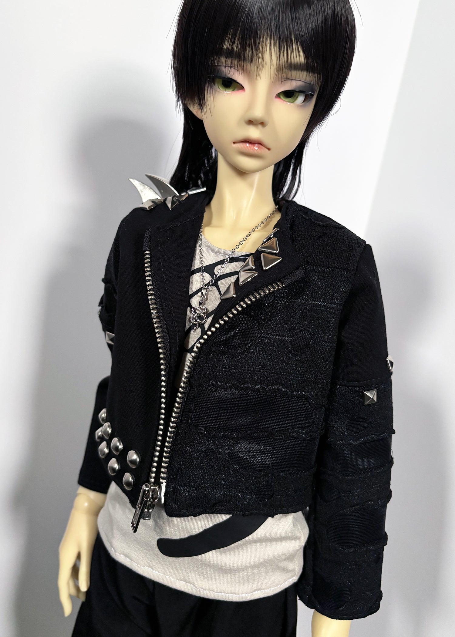 A doll wearing a black distressed zip-front jacket with silver studs and spikes, layered over a light gray top and black bottoms, photographed against a plain light background.