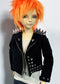 A doll with bright orange hair wearing a black studded moto jacket over a white ribbed top, photographed against a plain light gray background.