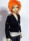 A doll  with bright orange hair wearing a black spiked jacket over a white ribbed top and dark pants, photographed against a plain light background.