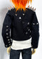 A black studded jacket with silver metal spikes on the shoulders and sleeves, worn by a doll with bright orange hair, a white ribbed shirt, and dark jeans against a plain white background.