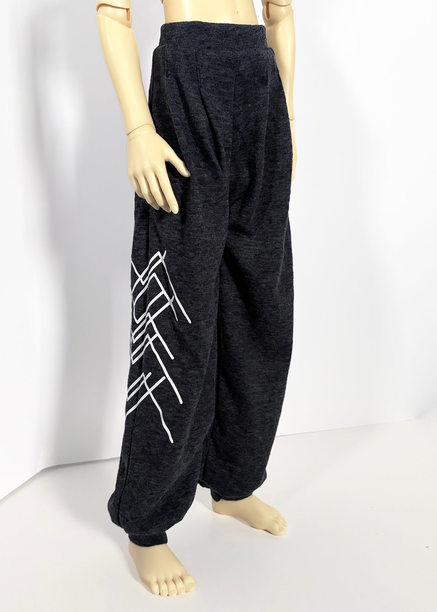 Dark charcoal gray wide-leg sweatpants with a white geometric mountain graphic on the left leg, displayed on a doll against a white studio background.