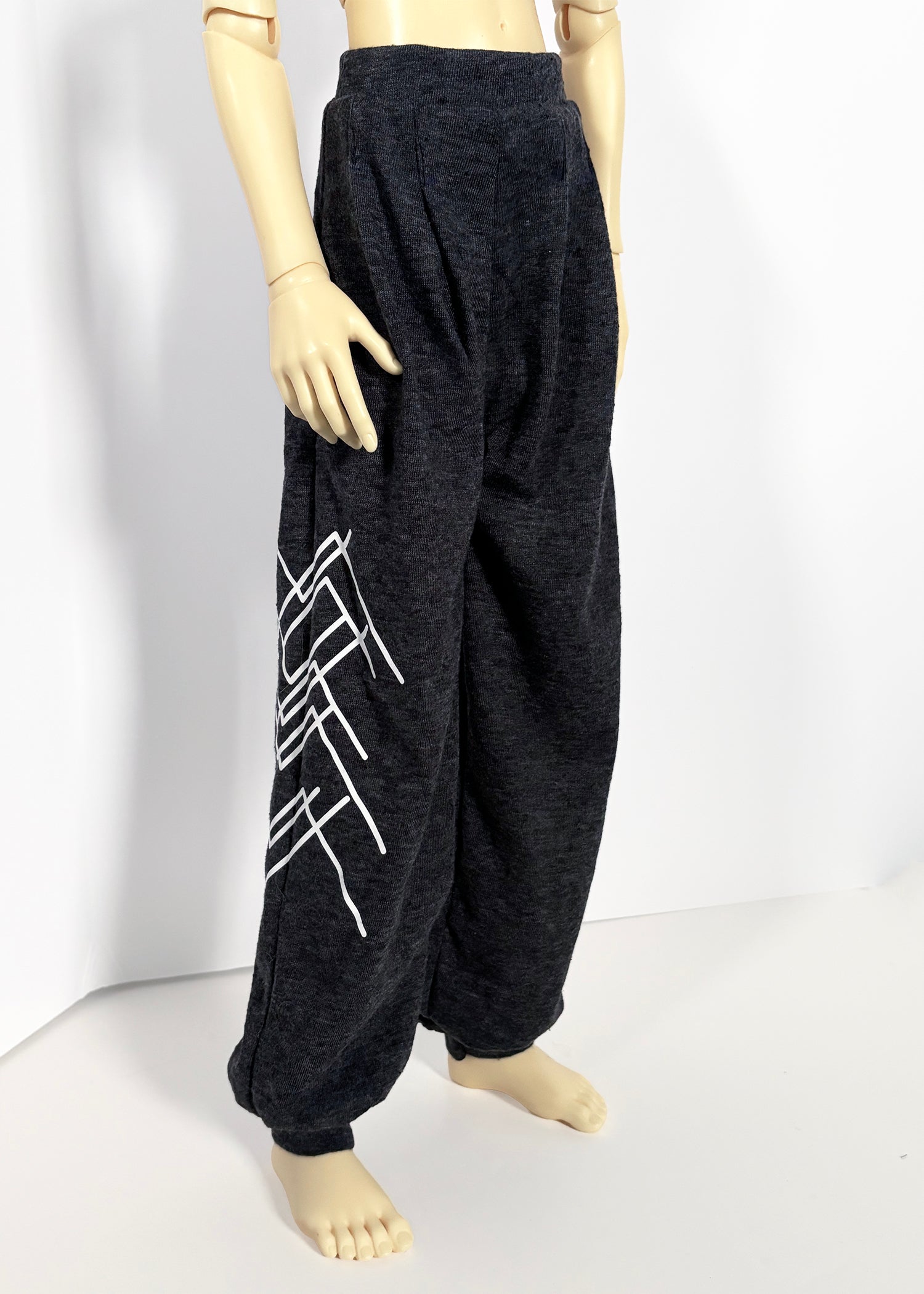 Dark charcoal gray wide-leg sweatpants with a white geometric mountain graphic on the left leg, displayed on a doll against a white studio background.