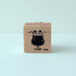 Wooden block stamp with a black illustration of a panda bear in a glass of soda on a light blue background
