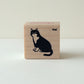 Rubber stamp with a sitting cat illustration on a beige wood block against a white background