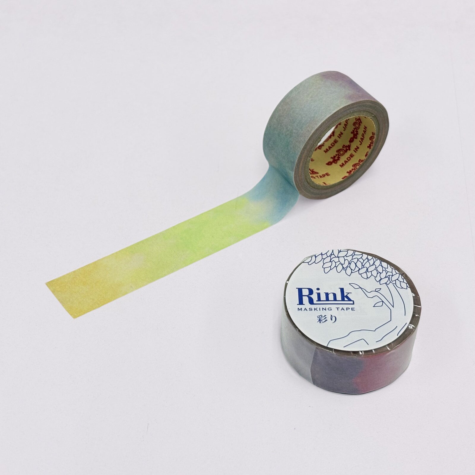 A roll of washi tape with a yellow-to-blue gradient strip unrolled, alongside another roll showing a blue-to-purple gradient, on a plain white background. The label on the bottom-right roll reads 'Rink Washi Tape'.