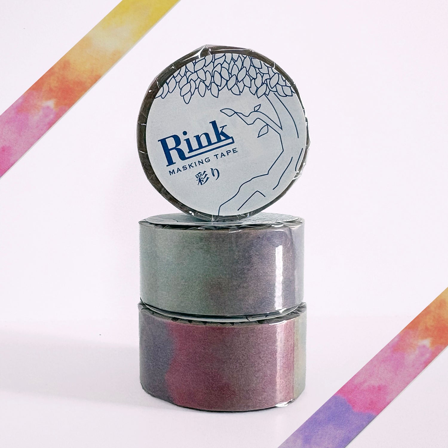Three rolls of Rink Masking Tape stacked vertically, with the top roll standing upright to show the label. The tape itself has a gradient rainbow pattern.