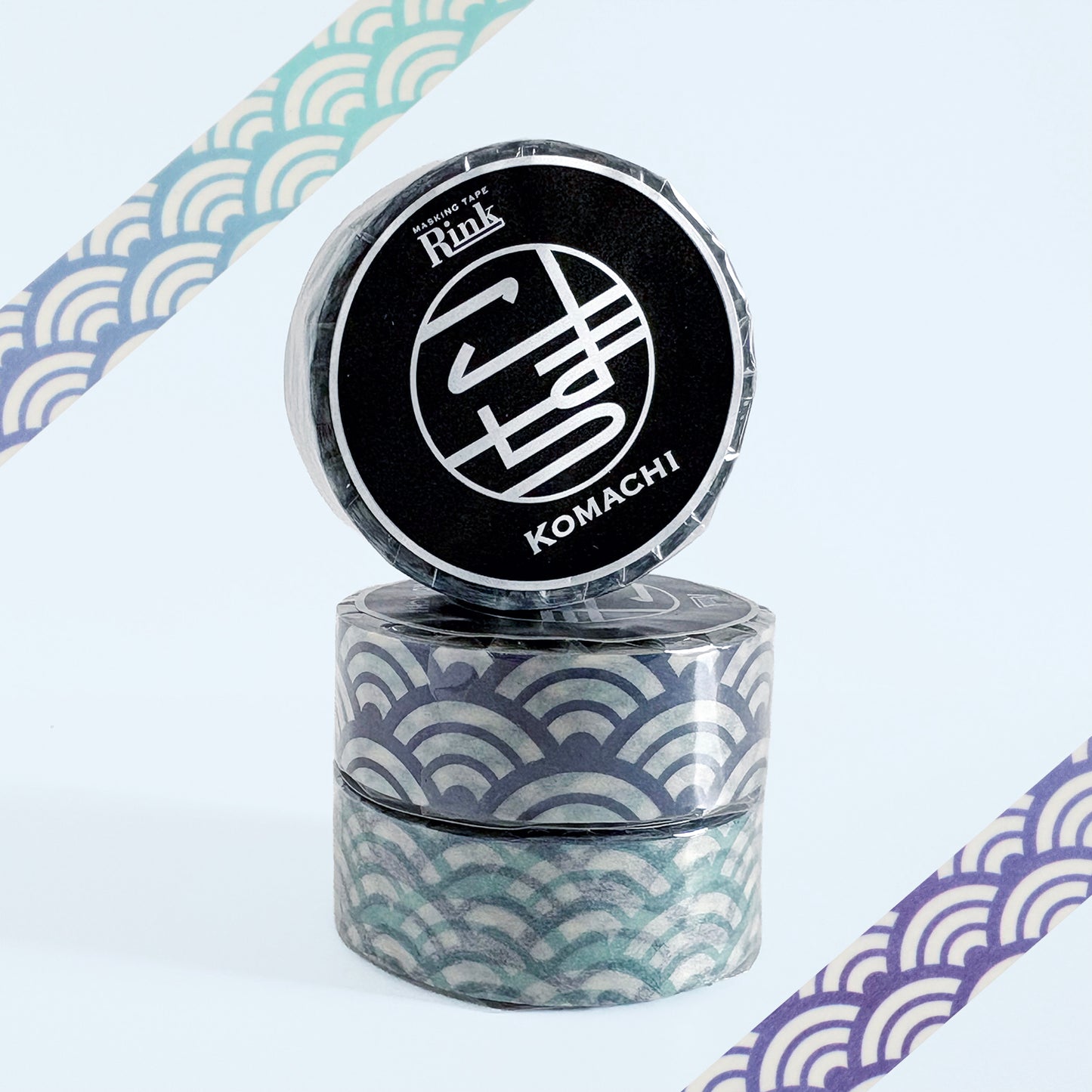 Three rolls of decorative washi tape stacked together, featuring a Japanese wave pattern in teal, blue, and white. The top roll is upright to reveal a black circular label with the brand name 'Rink' and the design name 'KOMACHI'.