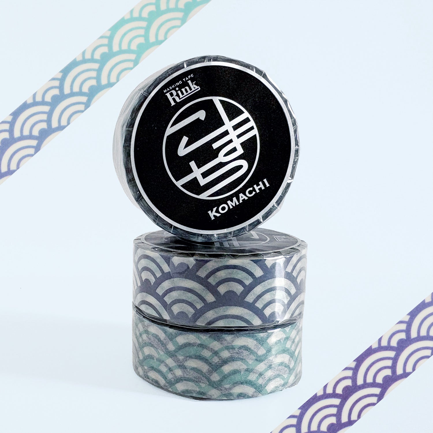 Three rolls of decorative washi tape stacked together, featuring a Japanese wave pattern in teal, blue, and white. The top roll is upright to reveal a black circular label with the brand name 'Rink' and the design name 'KOMACHI'.