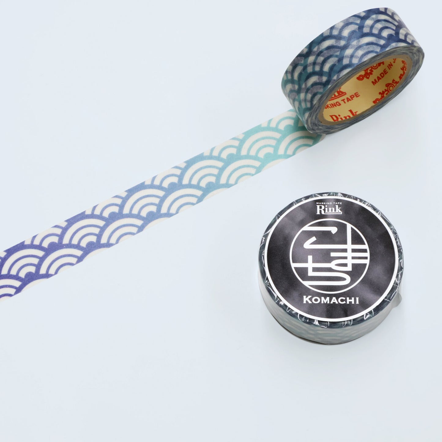 Two rolls of decorative washi tape on a white background, one showing a blue and white wave pattern with the rest of the roll visible, and the other showing a black and white Komachi label on the roll.