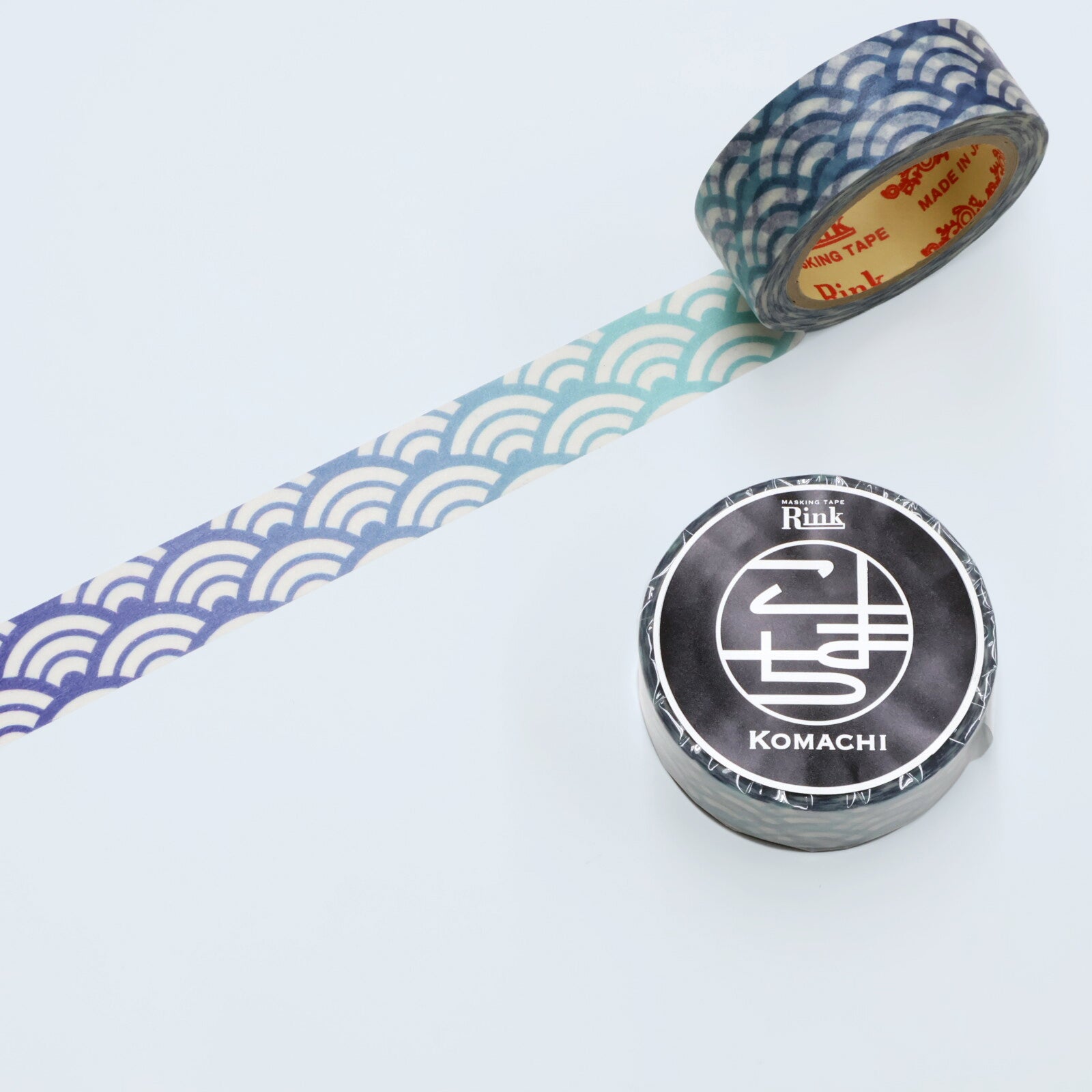 Two rolls of decorative washi tape on a white background, one showing a blue and white wave pattern with the rest of the roll visible, and the other showing a black and white Komachi label on the roll.